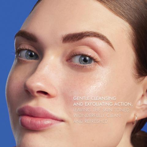Image GIF1 - A close-up of a persons face with clear, healthy skin, blue eyes, and a small hoop earring on the right ear, with the text GENTLE CLEANSING AND EXFOLIATING ACTION, LEAVING THE SKIN TONED, WONDERFULLY CLEAN AND REFRESHED.